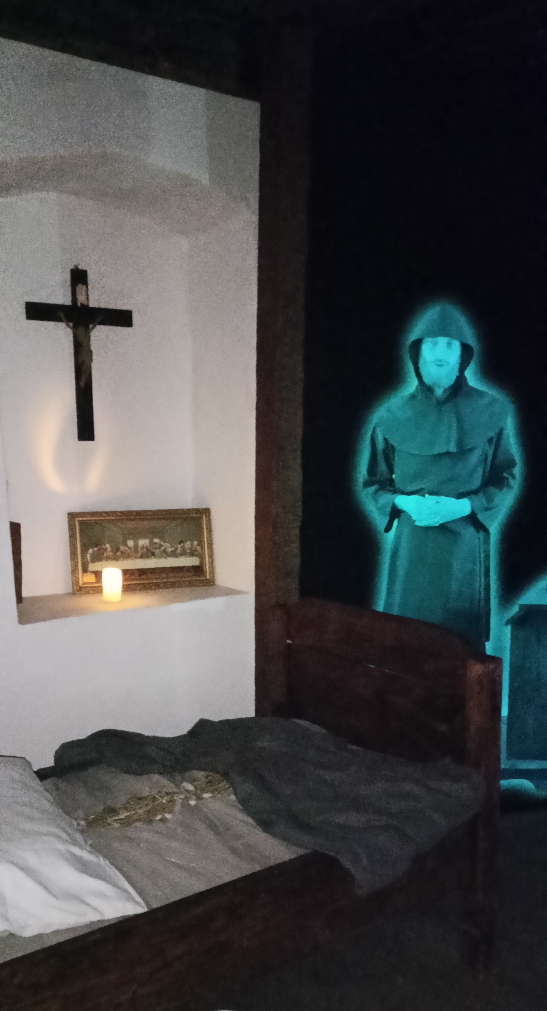 Scena w pokoju: krzyż, łóżko i duch mnicha w tle. Tajemnicza i gotycka atmosfera.